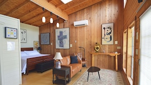Una habitación acogedora con cama, sofá, una mesita y una alfombra. Hay cuadros en las paredes y una ventana con persianas.