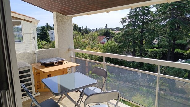 Ein Balkon mit Tisch, Stühlen, einem Grill und Blick auf Grünflächen und Gebäude.