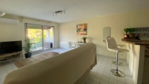 Ein Wohnzimmer mit Sofa, Fernseher, Essbereich mit Tisch und Stühlen sowie Küchenzeile mit Spüle und Arbeitsplatte.