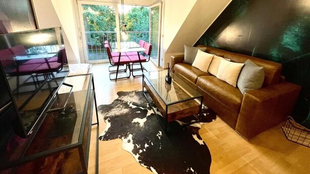 Una sala moderna con una mesa de centro de vidrio, un sofá de cuero y una zona de comedor con sillas rosas.