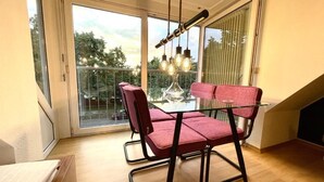 Un balcón con mesa de vidrio y sillas rojas, una lámpara colgante y vistas a árboles.