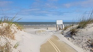 Een zandpad langs het strand leidt naar een loopplaats met een bord, met uitzicht op de oceaan.