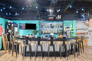 A bar area with a counter, stools, and a wall displaying various bottles and a sign.