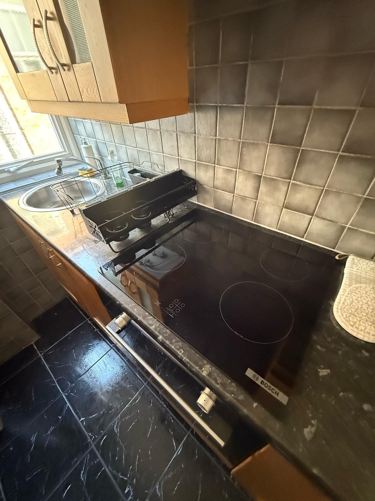 Une cuisine équipée d’une plaque de cuisson à induction Bosch, d’un évier et d’une fenêtre située au-dessus de l’évier.