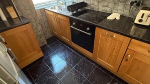 A modern kitchen with wooden cabinets, a black tiled floor, stainless steel appliances, and a window providing natural light.