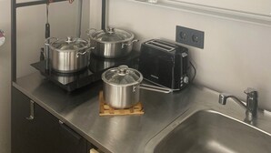 A compact kitchen with a sink, two stainless steel pots, a toaster, and hanging kitchen utensils.
