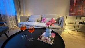 Una sala de estar moderna con un sofá, una mesita de centro con dos vasos de bebida roja y un jarrón con flores rosadas.