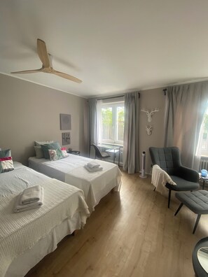 Una habitación con dos camas, ventilador de techo, una mesa con sillas, radiador y una decoración de cabeza de venado.