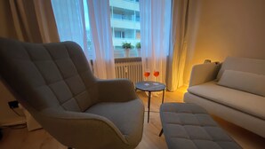 A modern living room with a grey armchair, a sofa, and a small round table with two glasses.