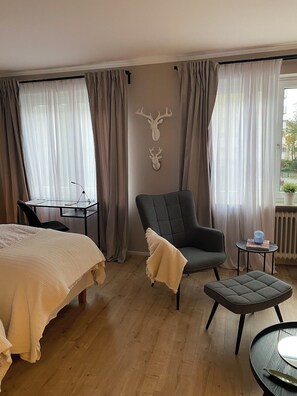 A hotel room with a bed, a chair, a small table, and a window with curtains.