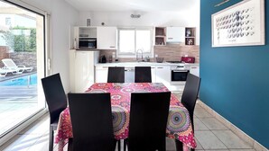 Une cuisine moderne avec des meubles blancs, une table à manger recouverte d’une nappe colorée et un mur d’accent bleu.