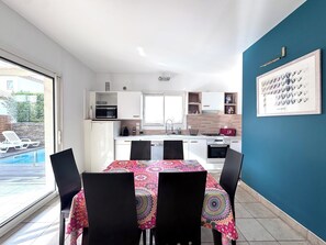 A modern kitchen with white cabinets, a dining table with a colorful tablecloth, and a blue accent wall.