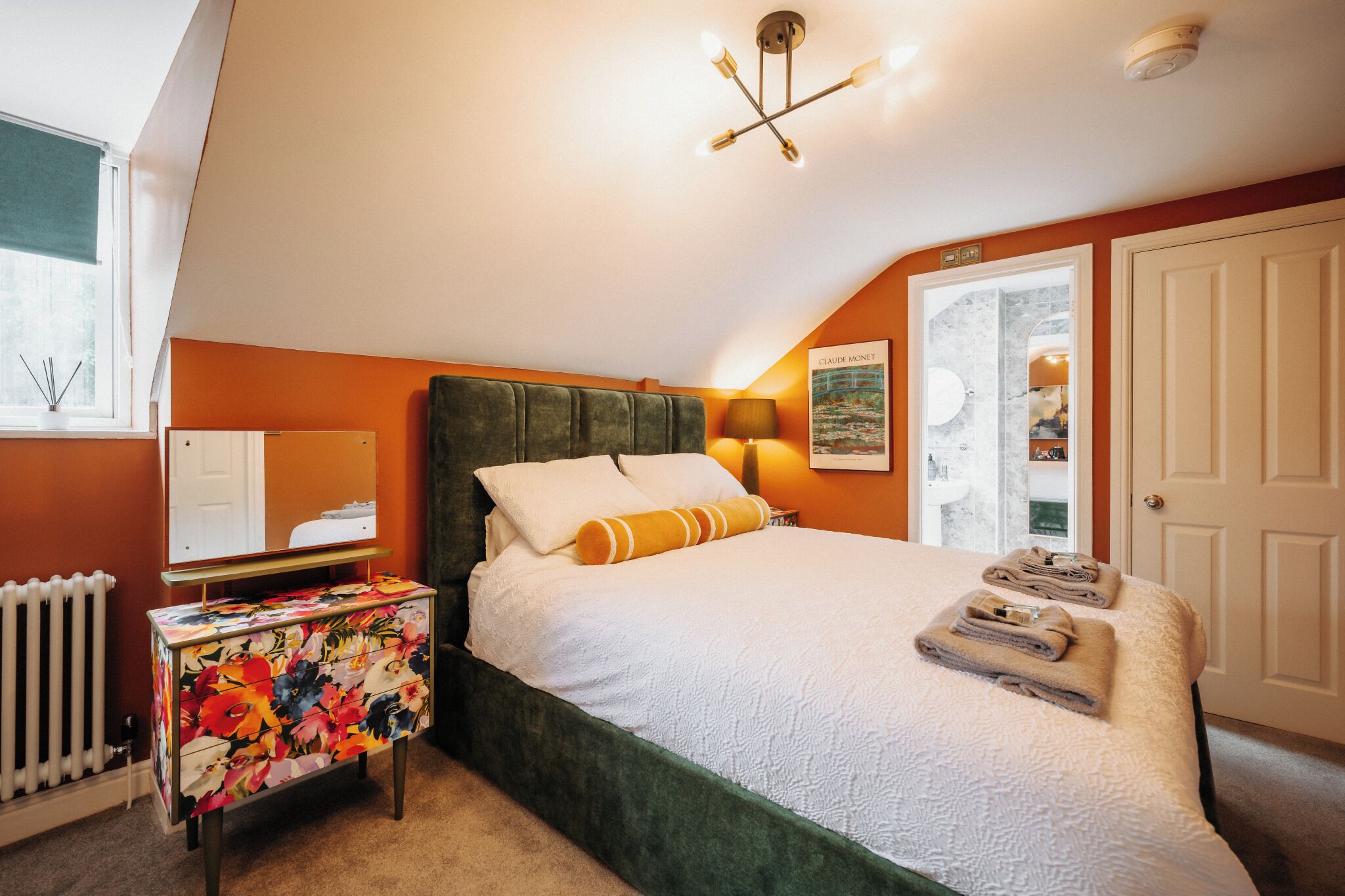 A bedroom with a green upholstered headboard, a white bedspread, and a side table with a floral pattern.