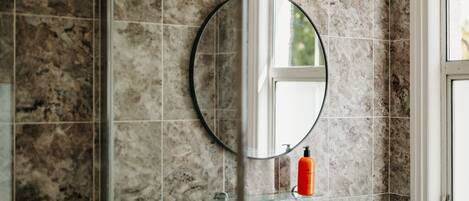 A bathroom with a round mirror, a glass shelf, and a window.