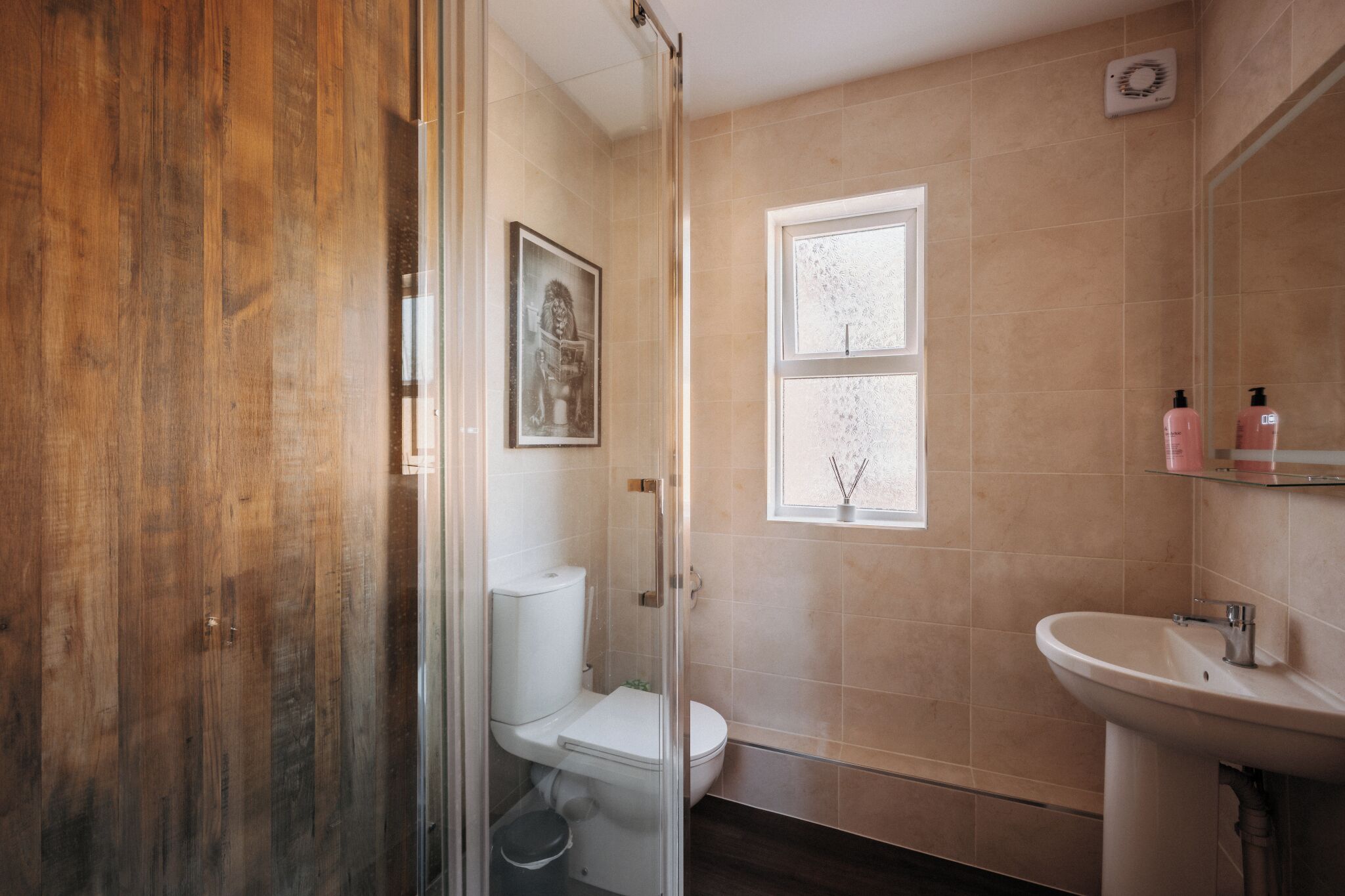 Un baño con suelo de madera, cabina de ducha de vidrio, inodoro, lavabo y ventana con vistas.