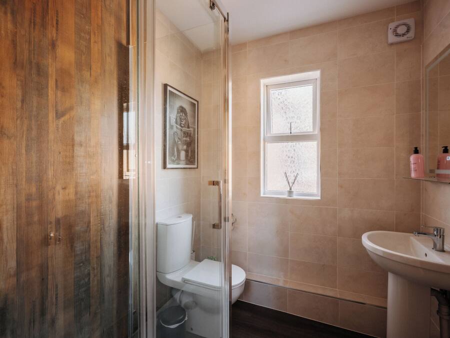 Un baño con suelo de madera, cabina de ducha de vidrio, inodoro, lavabo y ventana con vistas.