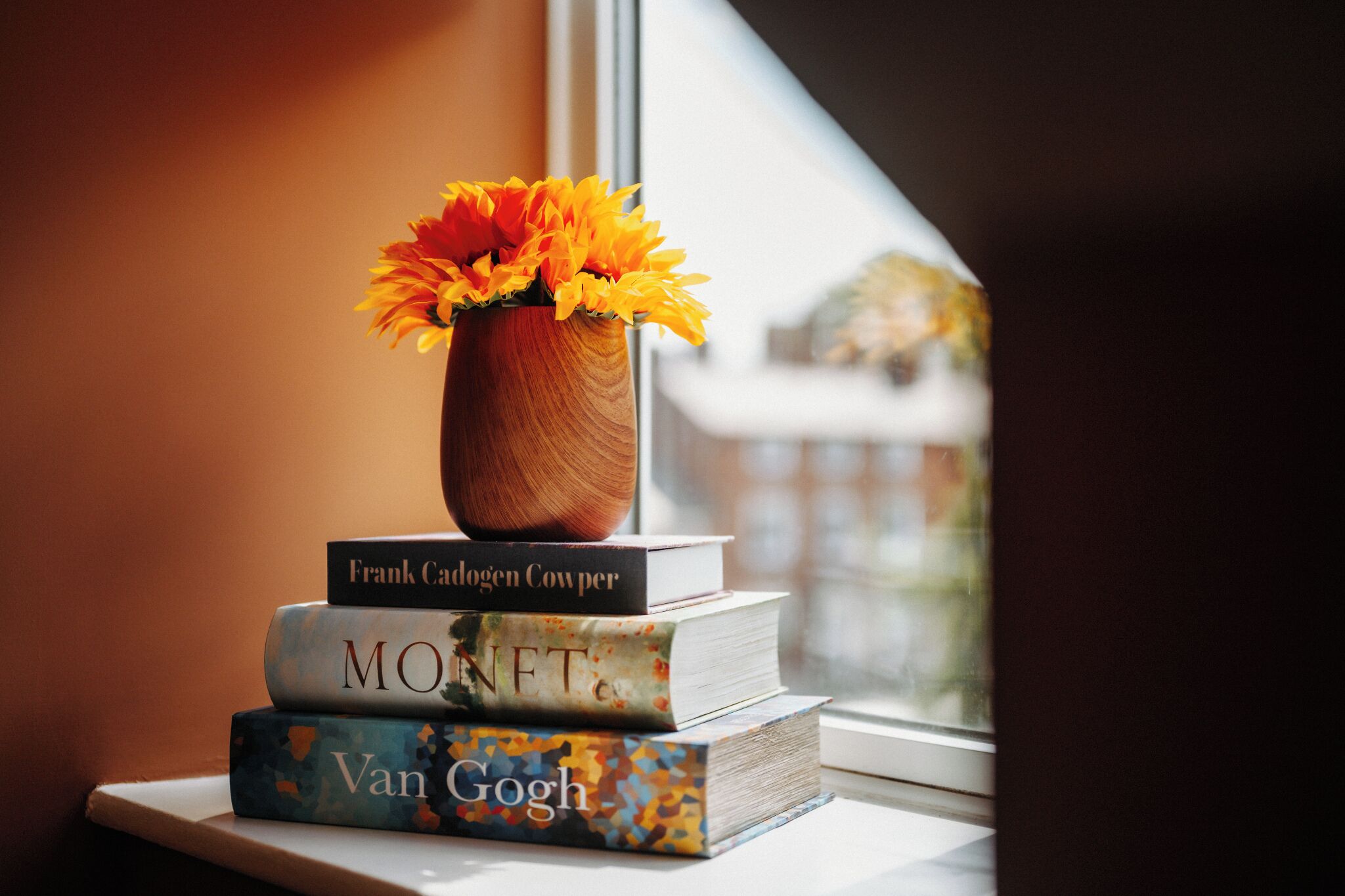 Una pila de libros con un florero encima, sobre un alféizar.