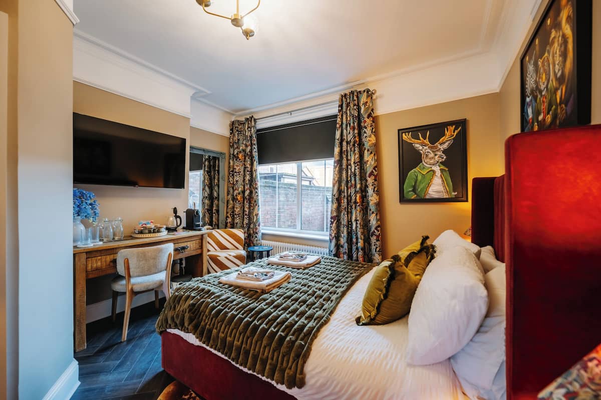 Ein Hotelzimmer mit Bett, Schreibtisch, Stuhl, Fernseher und einem Fenster mit Vorhängen.