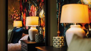 A bedroom with a bed, two bedside tables with lamps, a decorative vase, and a floral wall mural.