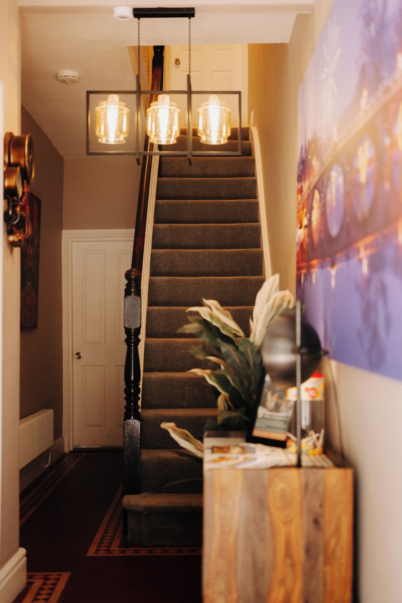 Eine Treppe mit Holzwand und Geländer, eine Wandleuchte und ein Blumentopf.