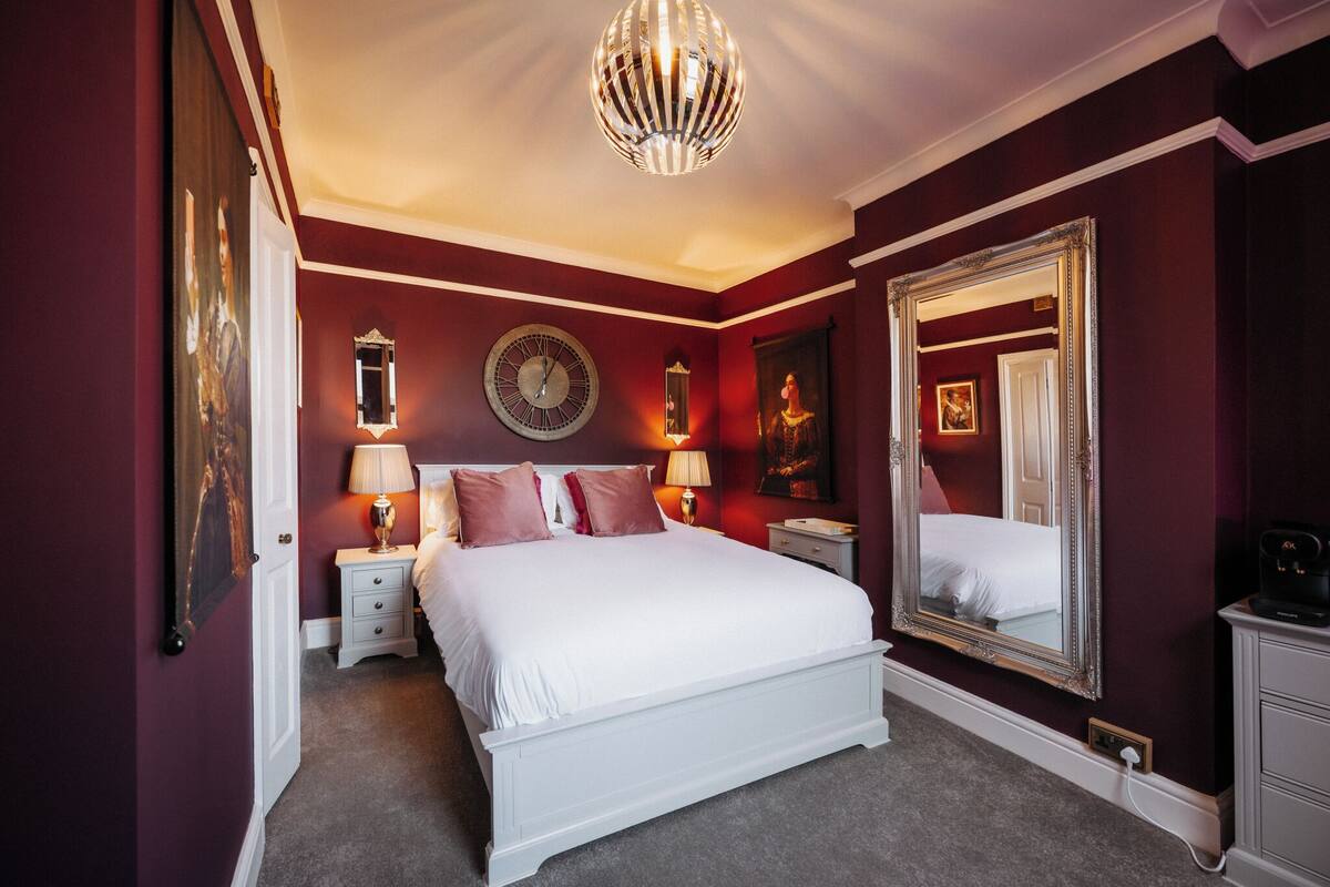 Ein Schlafzimmer mit einem großen Bett, einer runden Wanduhr, einem Spiegel und einem Chandelier.