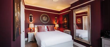 A bedroom with a large bed, a round wall clock, a mirror, and a chandelier.