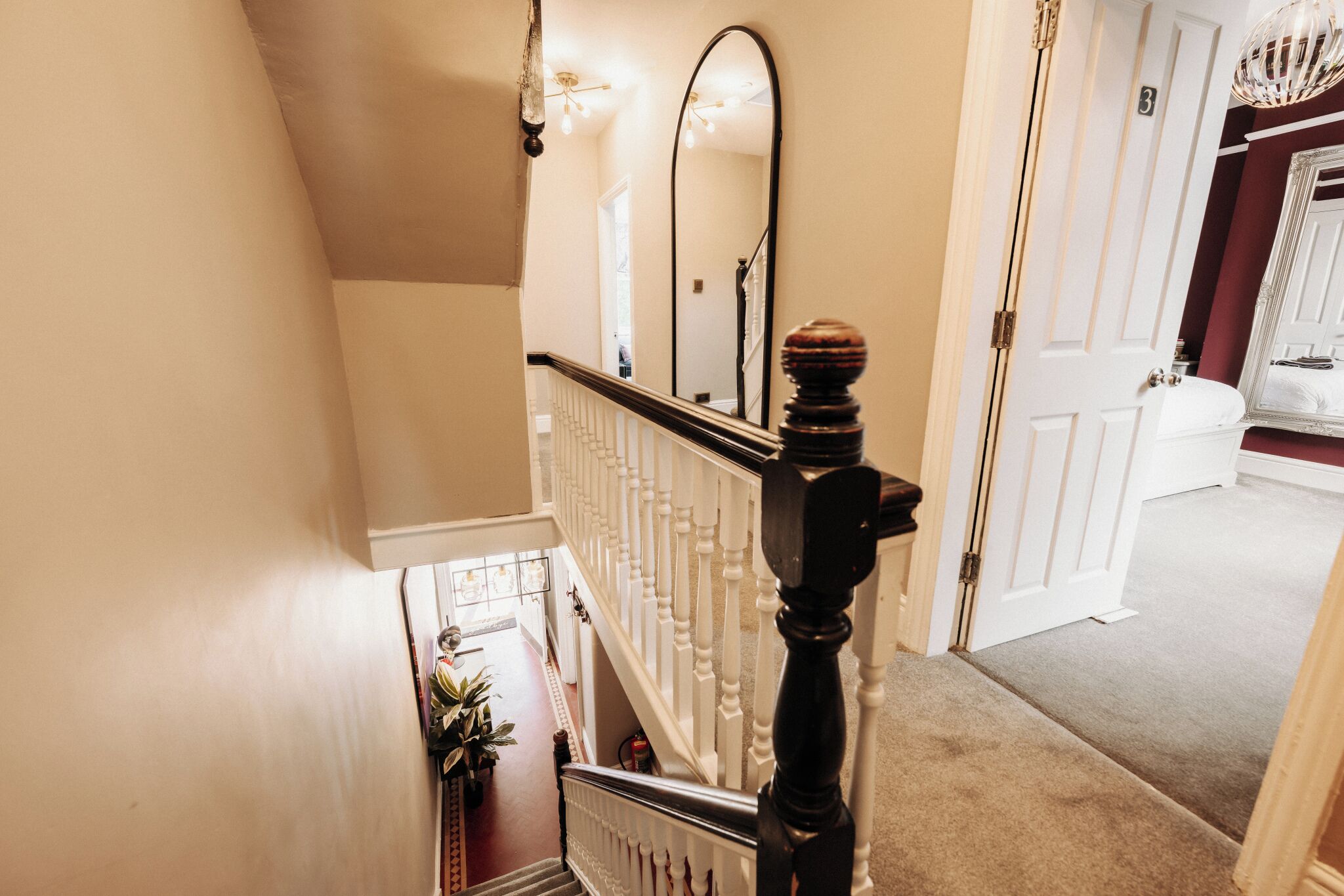 A staircase with a white railing and a wooden balustrade, leading to a room with a white door and a mirror on the wall.