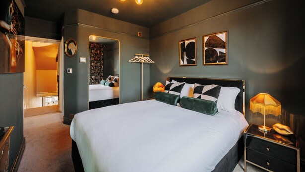 A modern bedroom with a large bed, a nightstand with a lamp, and a mirror. - Unique Shrewsbury Rooms (Shrewsbury)