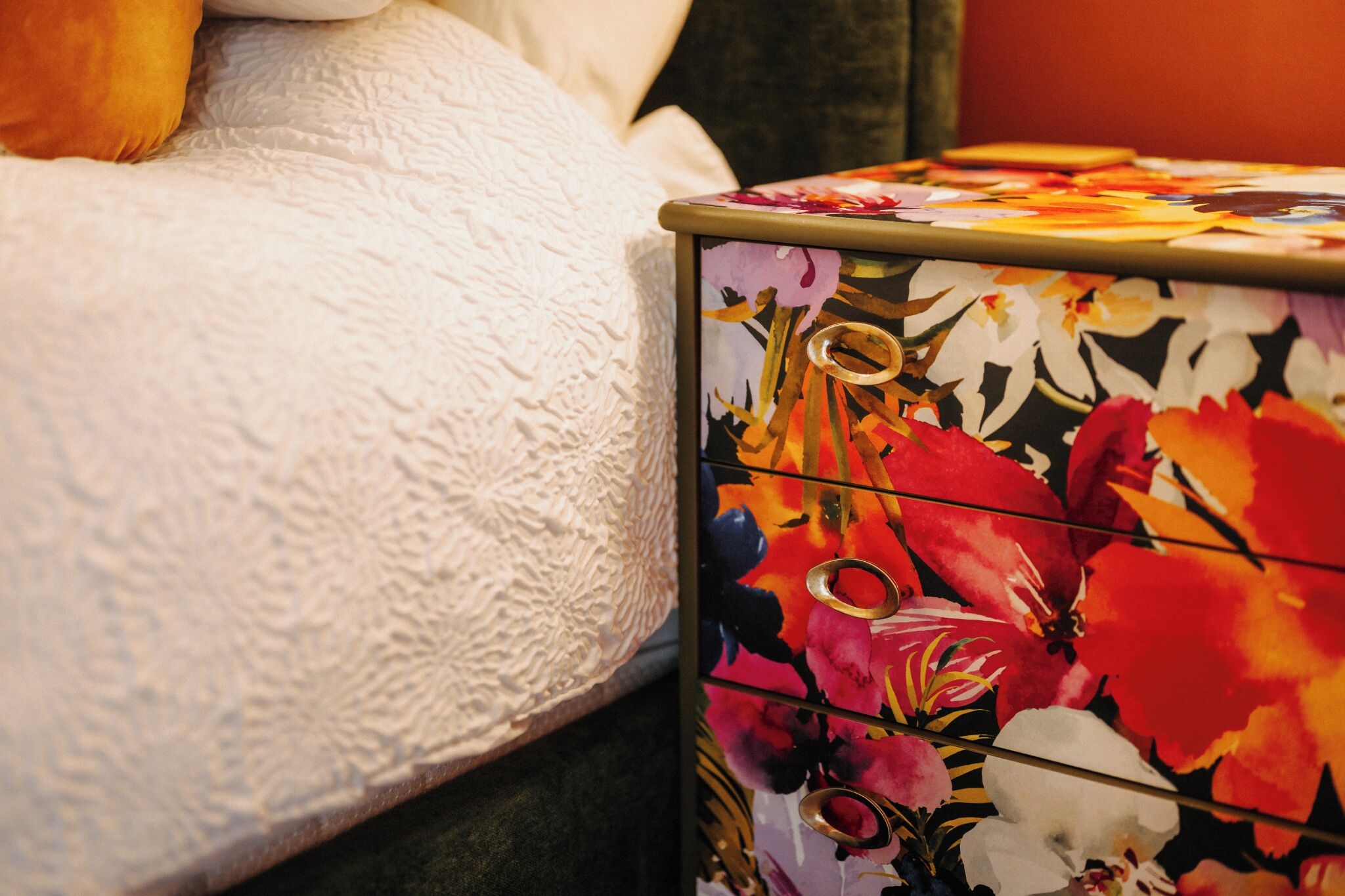 A bed with a textured white cover and a floral-patterned dresser with multiple drawers.