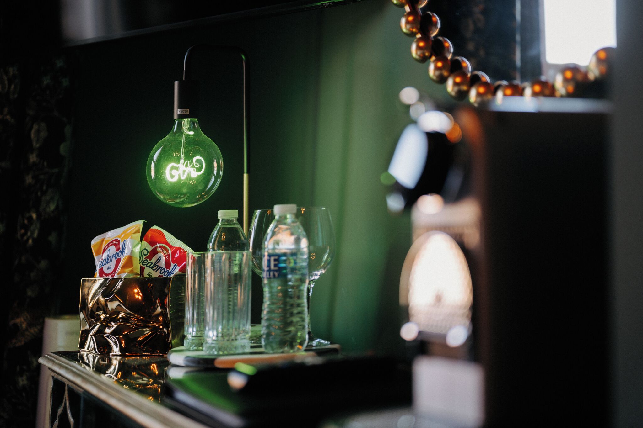 Uma área de bar com uma lâmpada verde pendurada, um copo com gelo e garrafas de água e refrigerante.
