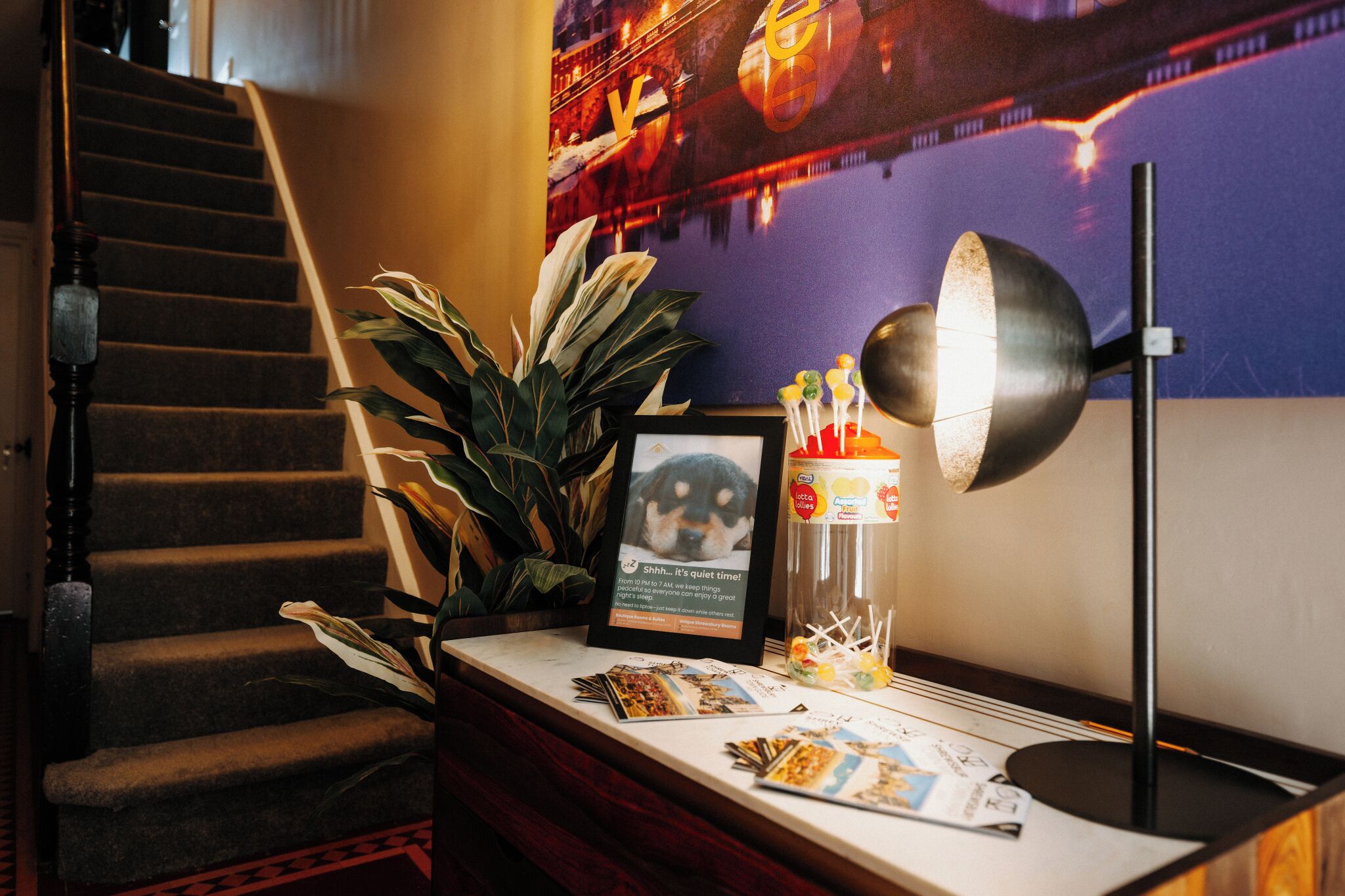 A reception desk with a framed photo, a plant, a lamp, and a glass jar with lollipops.