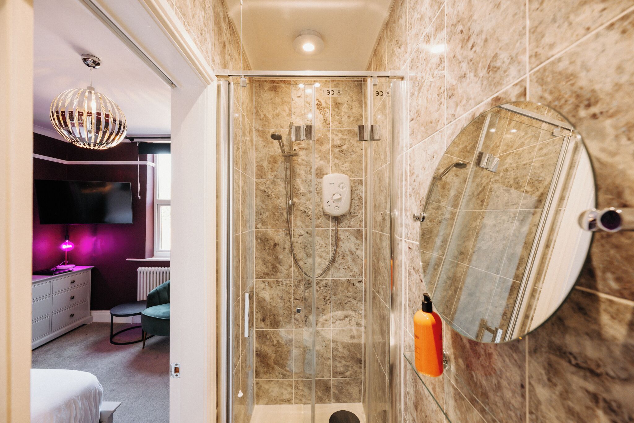 Un baño moderno con ducha de vidrio, azulejos de mármol, un espejo grande y un tocador con televisor.