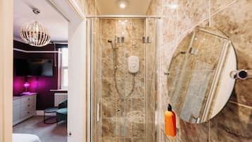 Un baño moderno con ducha de vidrio, azulejos de mármol, un espejo grande y un tocador con televisor.
