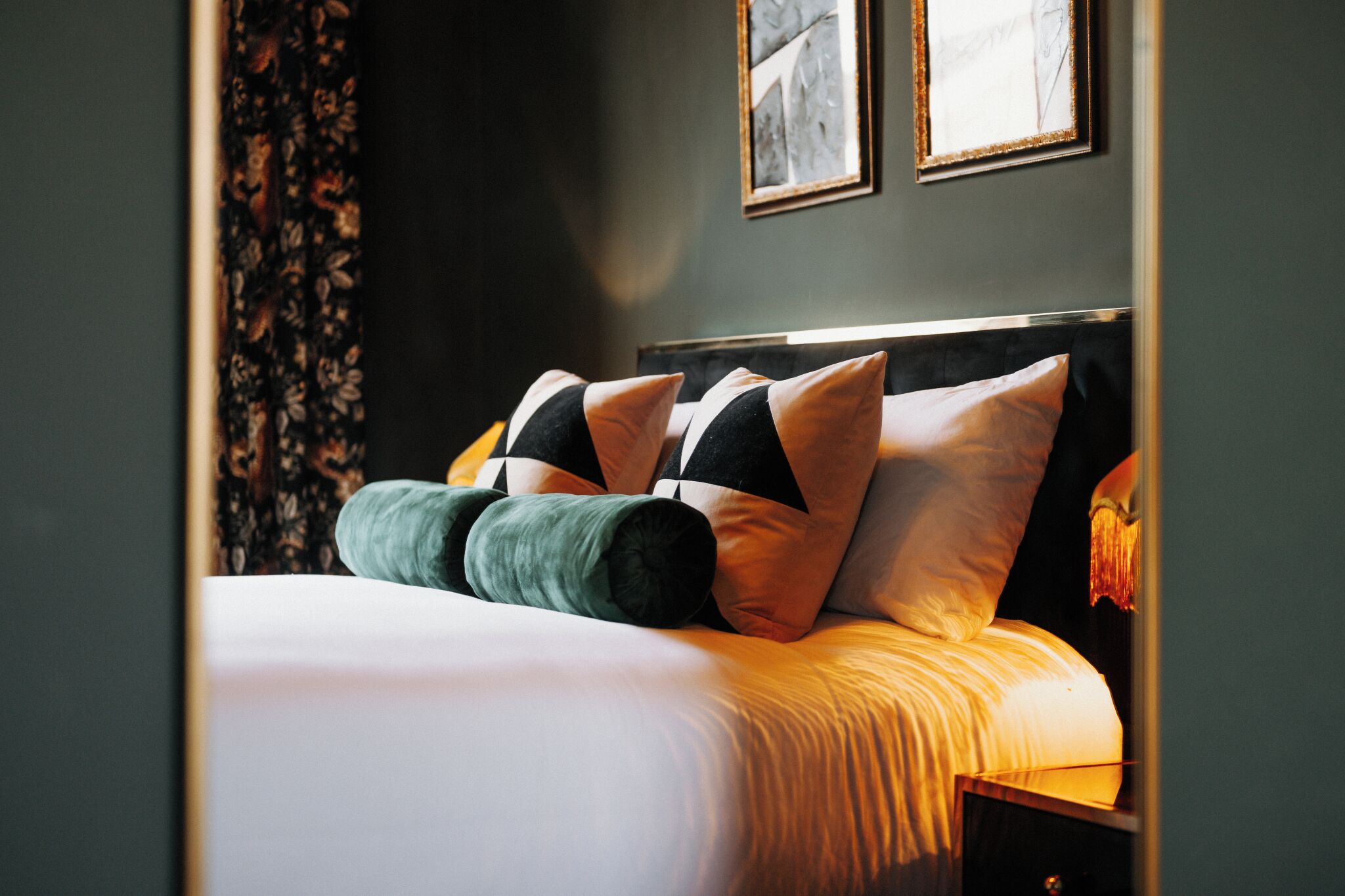 A neatly made bed with a white duvet and multiple pillows, including a green one.