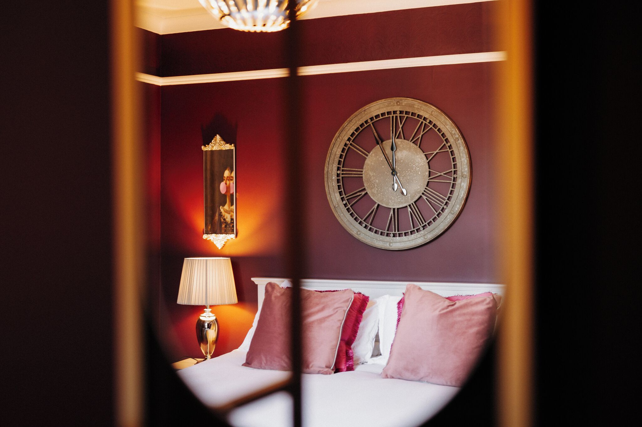A hotel room with a bed, a wall clock, a lamp, and a mirror.
