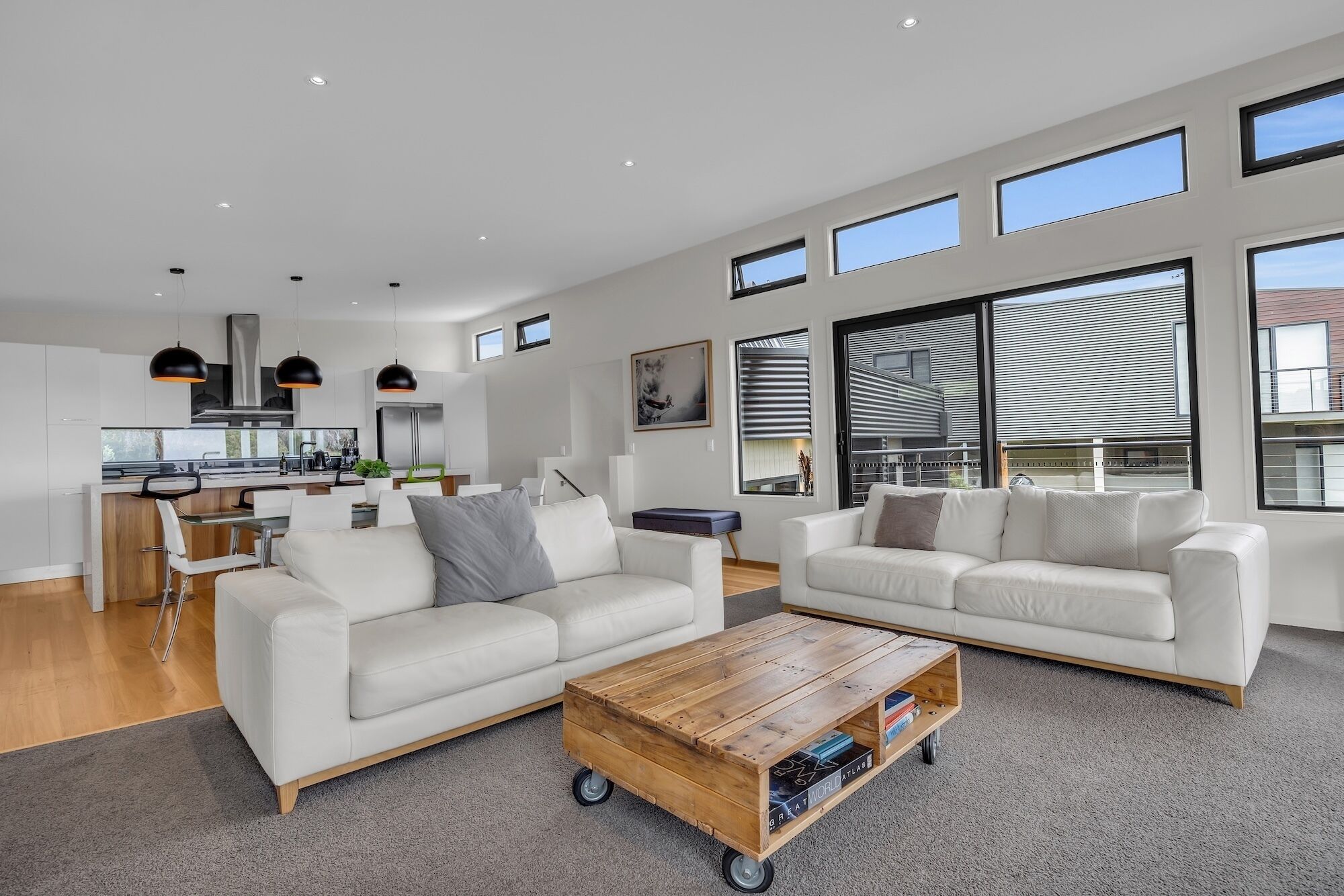 A spacious living area with two white sofas, a wooden coffee table, and a kitchen in the background.
