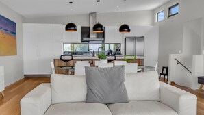A modern living room with a white sofa, a grey pillow, and a dining area with a glass table and chairs.