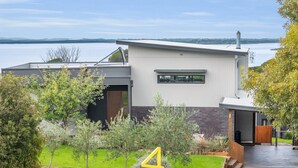 A modern two-story house with a garage, a small garden, and a view of a lake.