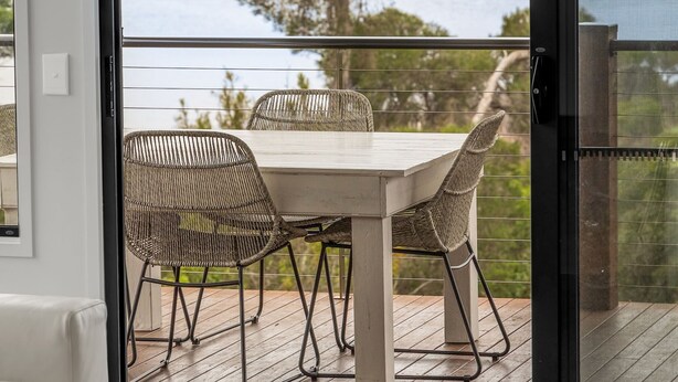 A balcony with a table and chairs, overlooking a body of water and a tree.