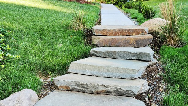 Un chemin de pierres qui traverse un jardin bien entretenu, avec de la pelouse et de petites plantes.