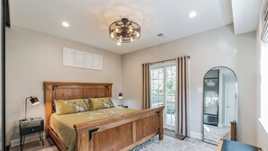 Une chambre avec un lit en bois, une table de chevet, une lampe de bureau, un miroir et une vue sur l’extérieur grâce à une porte coulissante.