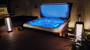 Un bain à remous doté d’un éclairage intérieur, entouré d’une terrasse en bois et de deux grands lanternes rectangulaires illuminées.