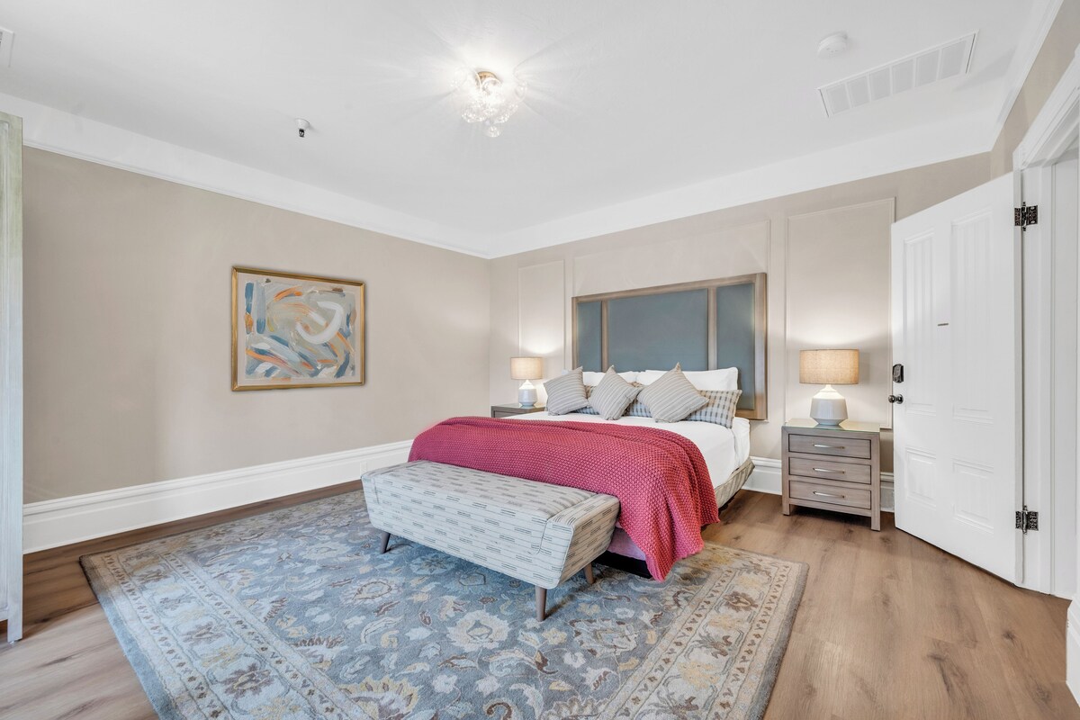 A bedroom with a large bed, a bench, a nightstand, and a door.