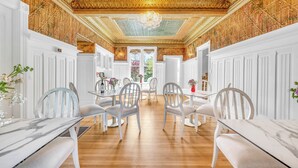 A dining area with white chairs and tables, a wooden floor, and a decorative ceiling with intricate patterns.