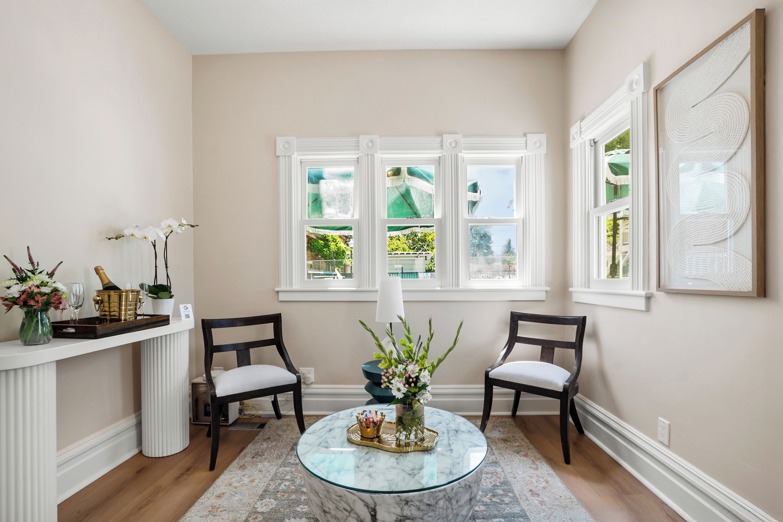 Une pièce comprenant une table basse en marbre, deux fauteuils, un vase avec des fleurs, une bouteille de champagne et un plateau décoratif.