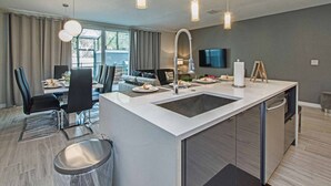 Une cuisine moderne dotée d’un îlot central, d’appareils électroménagers en acier inoxydable et de luminaires suspendus.