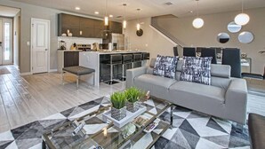 Un salon moderne avec un canapé gris, une table basse et une cuisine en arrière-plan.