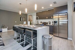 A modern kitchen with a central island, stainless steel appliances, and bar stools. - 4BD Sunshine Spot with Pool BBQ and Parks Around (Kissimmee)