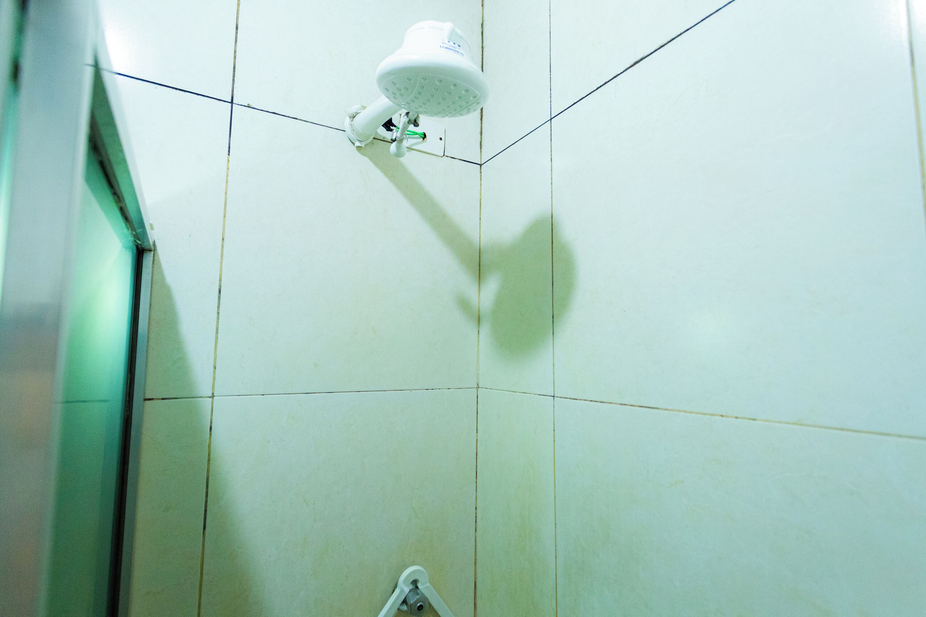 A corner of a bathroom with white tiles and a shower head mounted on the wall.