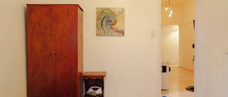 Un dormitorio con un armario de madera, una mesita de noche pequeña, un cuadro en la pared y un baño visible a través de una puerta abierta.